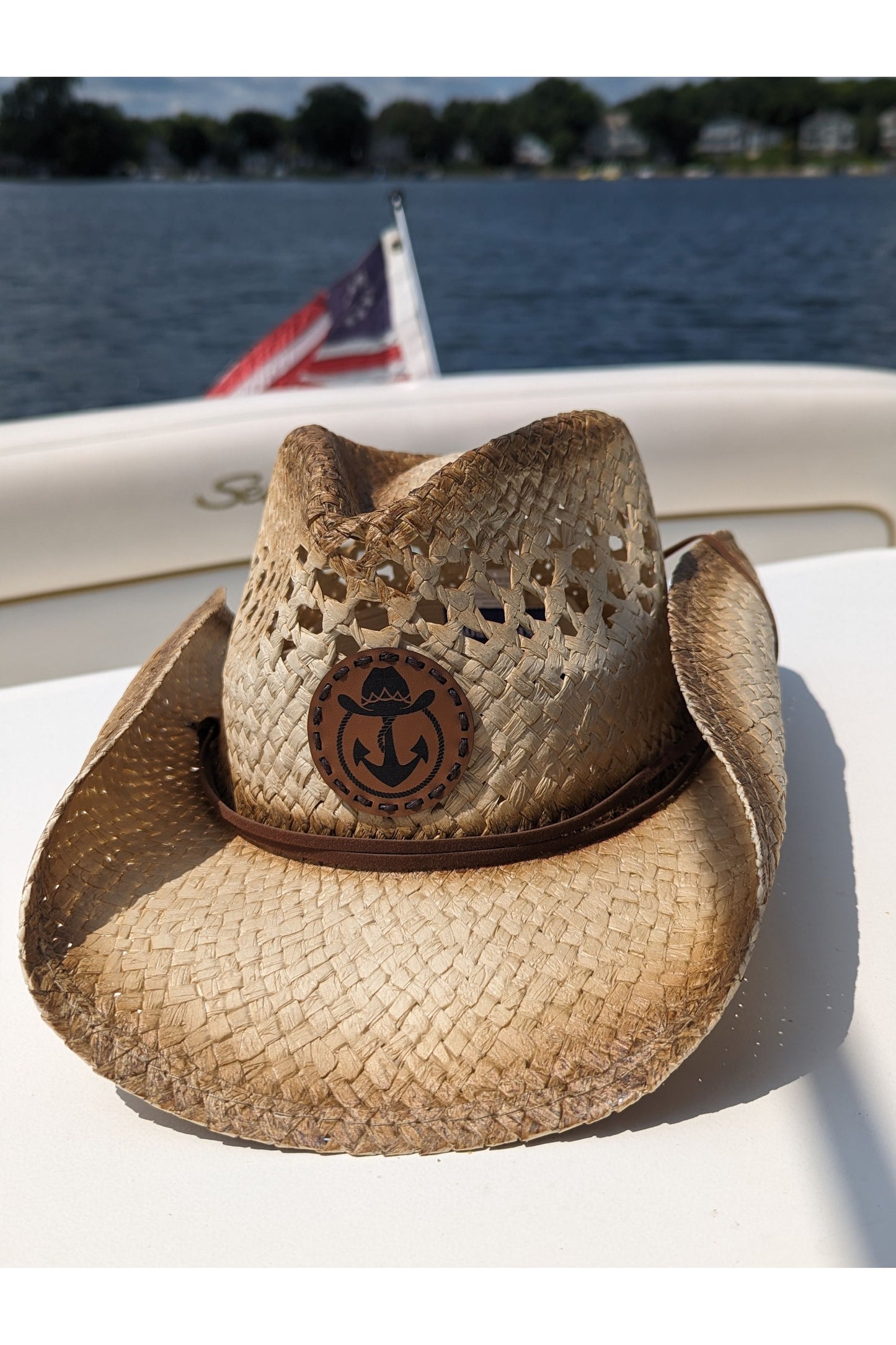 Photo of a Lake Cowboy Signature Cowboy Hat with the iconic hat, lasso and anchor logomark on the front of the hat. The hat is shown sitting on a table on a boat with the American flag in the background. The photo was taken on Lake Minnetonka, MN.