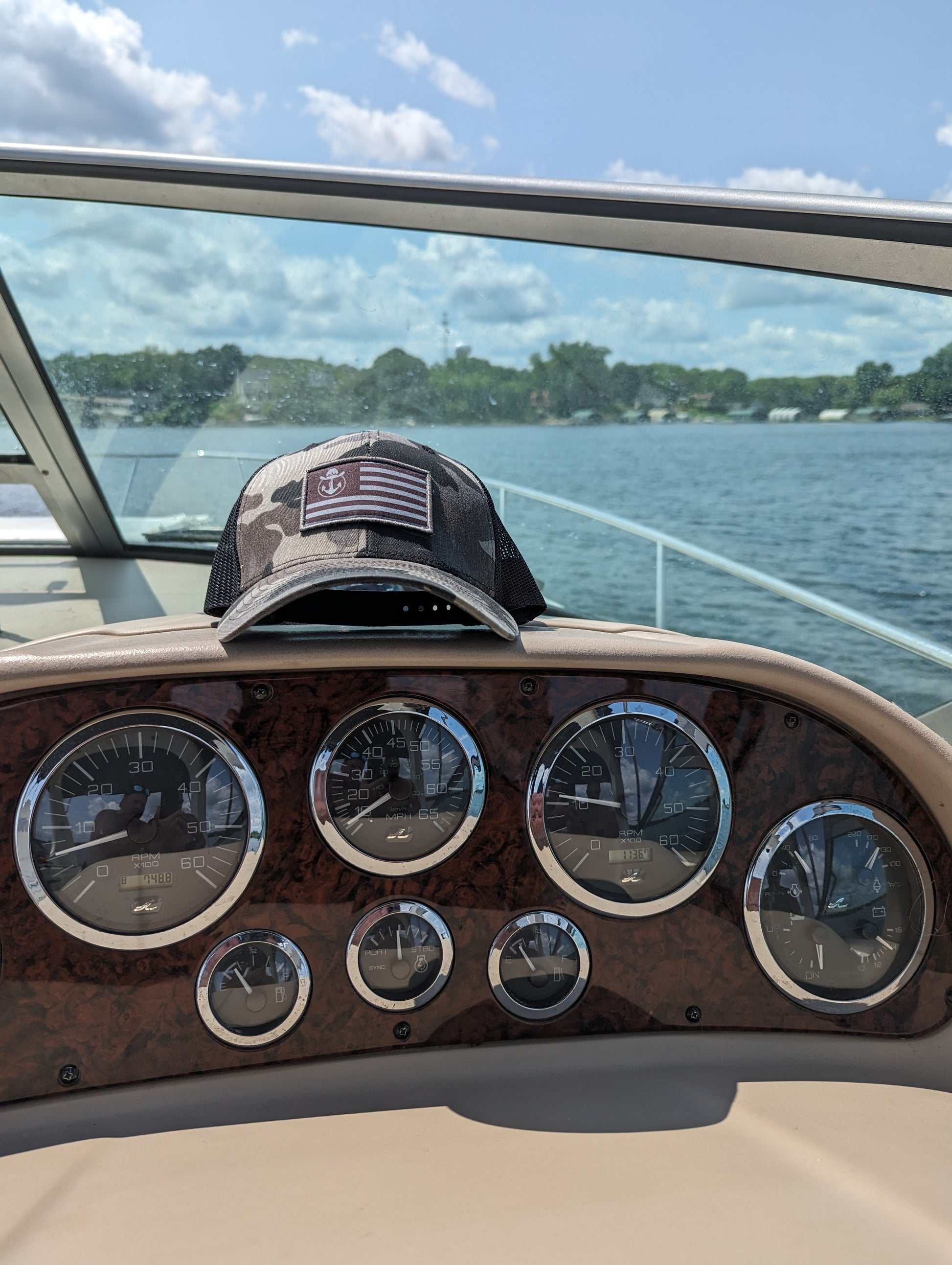 Photo of a Lake Cowboy Camo Baseball Hat (with Patriot Flag) shown on a boat console. Photo taken on Lake Minnetonka.