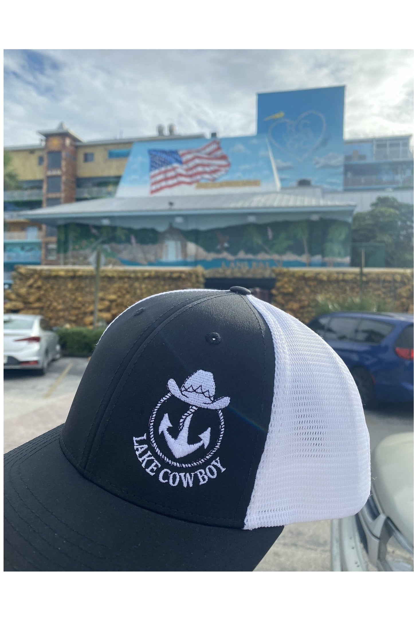 Photo of a Lake Cowboy Baseball Hat (Black & White) in front of a Flag Mural at JJ Hill Days in Wayzata, MN